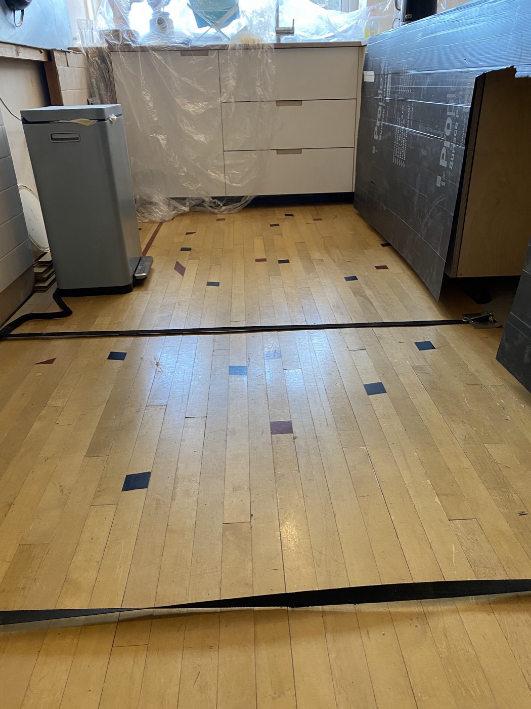 An old maple strip floor, mid-lift — years of line markings and wear about to be sanded away.